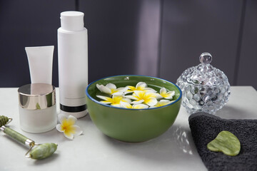 Beautiful spa composition with plumeria flowers. Face roller and guasha massager. Facial skin care, anti age products and creme. Chinese Gua Sha massage tools.