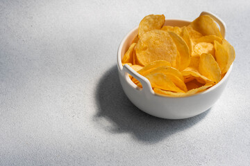 Crispy salty potato chips or crisps in bowl on white background. Unhealthy food concept.