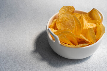 Crispy salty potato chips or crisps in bowl on white background. Unhealthy food concept.