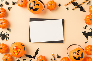 Top view photo of halloween decorations pumpkin baskets candy corn straws spiders cobweb bats cat silhouettes black envelope and white sheet in the middle on isolated beige background with empty space