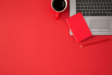Top view photo of small red closed organizer on laptop red pencil and cup of coffee on isolated red...