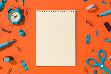 Top view photo of open spiral copybook and school accessories blue stationery on isolated orange background with blank space