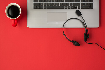 Top view photo of grey laptop red cup of coffee and black wired headphones with microphone on...