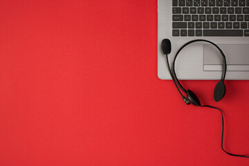 Top view photo of grey laptop and black wired headset with microphone on isolated red background with copyspace