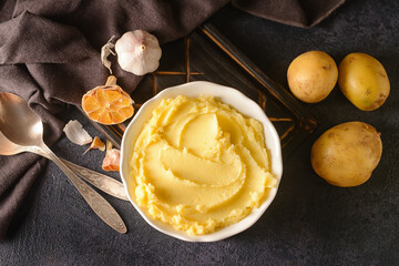 Bowl of tasty mashed potatoes with garlic and vegetables on dark background