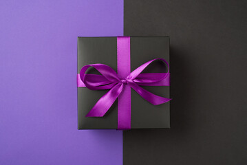 Top view photo of black giftbox with purple ribbon bow on isolated bicolor violet and black background with copyspace
