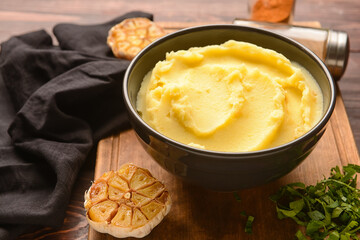 Bowl of tasty mashed potatoes with garlic on wooden background