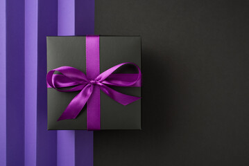 Top view photo of black giftbox with purple ribbon bow on isolated bicolor violet and black background with copyspace