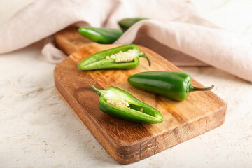 Board with cut green jalapeno peppers on light background, closeup