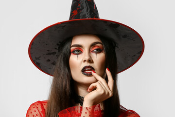 Beautiful woman dressed as witch for Halloween on light background