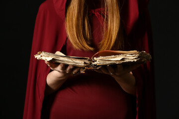 Young witch with spell book on dark background, closeup
