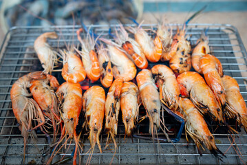 A large number of shrimps were grilled on a charcoal grill, turning orange and almost ready to eat.