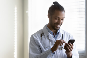 Smiling millennial generation african american biracial gp doctor physician using cellphone,...