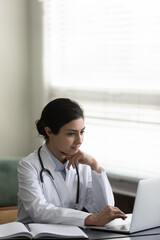 Vertical image focused young indian ethnic biracial woman gep doctor therapist working on computer...