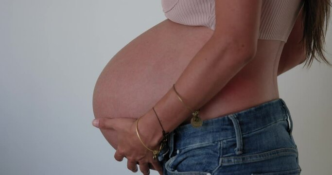 Large 9 month pregnant woman holds belly in front of neutral background