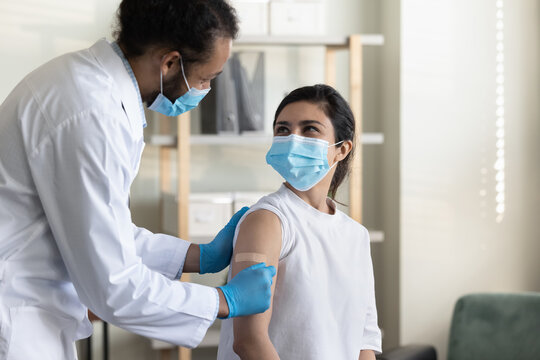 Happy Friendly Young African American Physician Family Doctor In Medical Uniform Gluing Patch On Hand Of Smiling Indian Ethnicity Woman After Injection, Finishing Anti Covid Vaccination In Clinic.