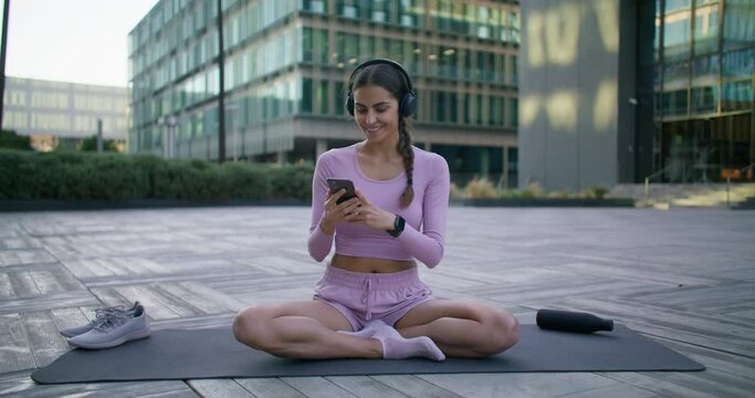 Millennial girl calls friend says happily hello shows different exercises for sport does workout in city enjoys new application for making conference makes selfie records video for fitness blog