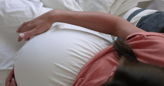 Pregant woman belly from above as she relaxes on a bed - close up on hands
