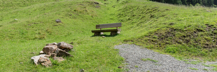 Empty wooden bench to rest on the green meadow in the mountains. Panoramic image