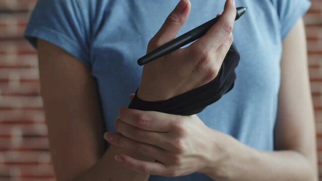White woman kneads her hand with pen for graphic tablet in special glove. Closeup. Concept of fatigue and hand pain
