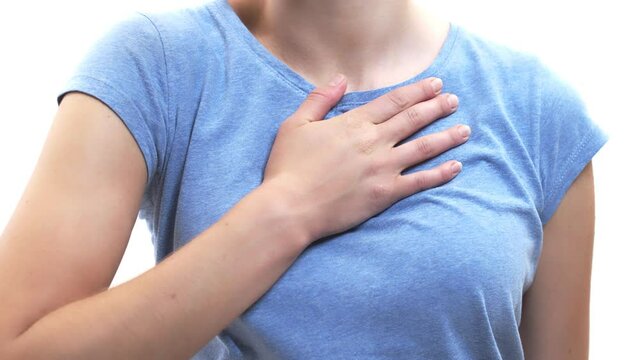 White woman puts her hand to her chest and squeezes, then adds second hand, closeup. Studio. Concept of cardiovascular diseases.