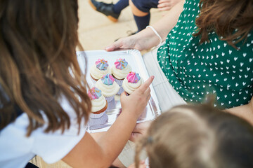 Schoolmates taking cupcakes from a tray held by the teacher