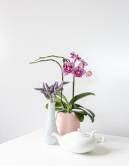 Vertical closeup of purple phalaenopsis orchid, lavender and white teapot on table with copy space