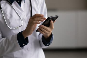 Close up young female medical worker general practitioner doctor nurse using smartphone applications, typing message giving distant online healthcare consultation to patients, telemedicine concept.