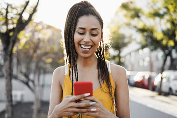 Bohemian mixed race girl using mobile phone outdoor with city in background - Focus on face