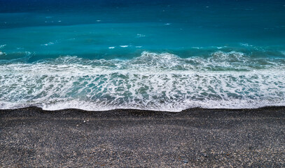 Sea shore background with black sand and pebbles and breaking wave, high angle perspective