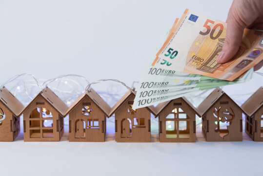 Lovely wooden houses, Christmas garlands, stand in a row. In the foreground is the hand holding the euro. Home purchase concept. Investments in real estate