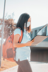 Niña joven estudiante con mascarilla en la escuela revisando apuntes y su carpeta