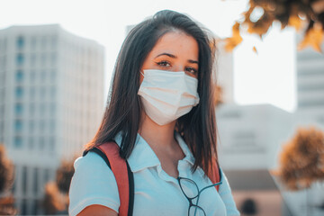 Chica joven feliz con mascarilla en su centro universitario con mochila junto a los arboles