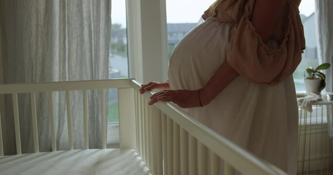 Pregnant woman looks over baby room and crib waiting for baby to come - mothers