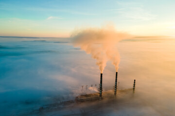 Naklejka na ściany i meble Aerial view of coal power plant high pipes with black smoke moving up polluting atmosphere at sunrise.