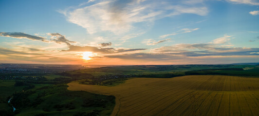 Aerial landscape view of yellow cultivated agricultural field with ripe wheat on vibrant summer evening.