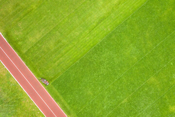 Obraz premium Aerial view of small figure of worker cutting green grass with mowing mashine on football stadium field with red running tracks in summer.