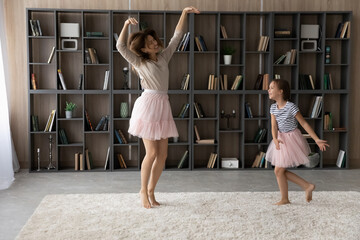 Happy crazy funky young mother and small child daughter in puffy skirts dancing to music in modern...