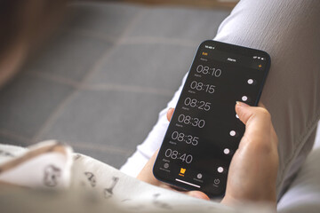 Woman set alarms for wake up on her mobile phone sitting on sofa at home