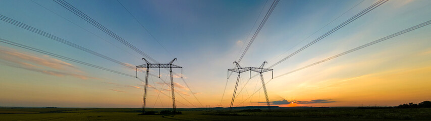 Dark silhouette of high voltage towers with electric power lines at sunrise.