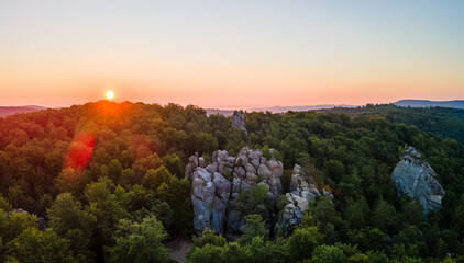 Vibrant foggy evening over dark forest trees and large rocky formations at bright summer sunset. Amazingl scenery of wild woodland at dusk.