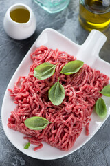 Close-up of fresh uncooked ground beef meat with condiments on a shovel-shaped plate, vertical...