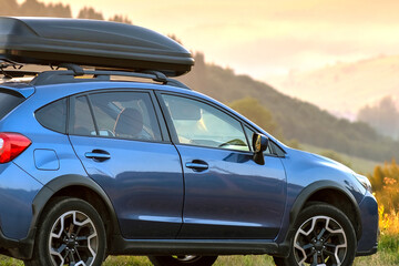 SUV car with roof rack luggage container for off road travelling parked at roadside at sunset. Road...