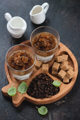 Wooden serving tray with coffee granita, coffee beans and sugar, vertical shot on a dark brown stone background