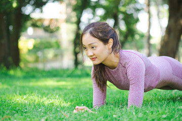 Naklejka na ściany i meble Young Asian woman doing yoga fitness exercises in the nature park, Exercise for health or warm-up body, fresh air, or Oxygen in the green tree in the park in sunlight.