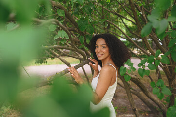 Fashion close up portrait of laughing attractive young naturally beautiful African American woman with afro hair and perfect teeth smile posing in nature parkland in green foliage