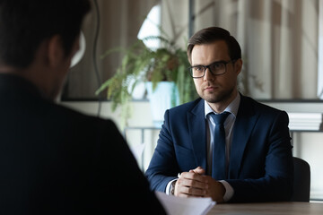 Confident man wearing glasses and suit candidate waiting for hr manager decision at meeting, job interview concept, hiring process, recruiter employer reading resume cv, considering application