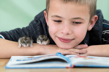 Close up portrait of smiling little boy reading book with small pet hamsters. Concept of studying...