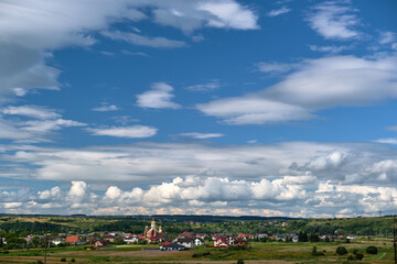 Bright landscape of white puffy cumulus clouds on blue clear sky over rural area.