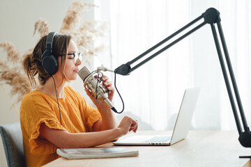 Female podcaster recording her podcast using microphone and laptop at his home broadcast studio....